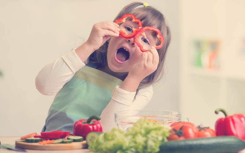 niña cocinando con verduras sonriendo