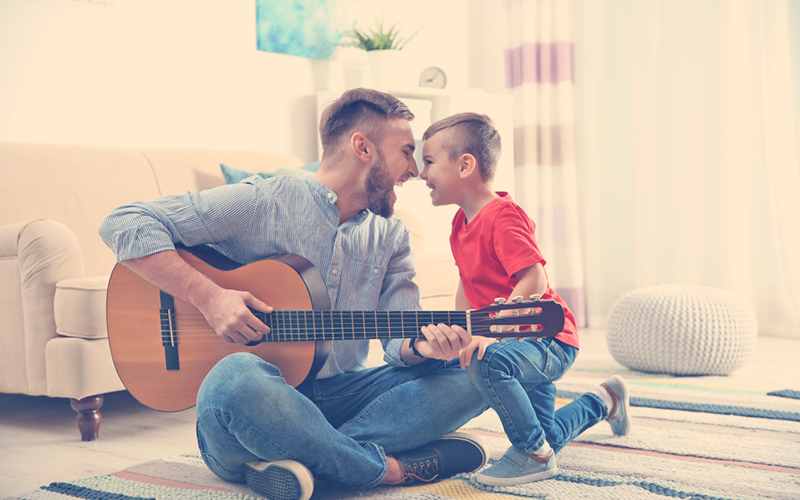 Papa divirtiéndose con su hijo mientras toca la guitarra 