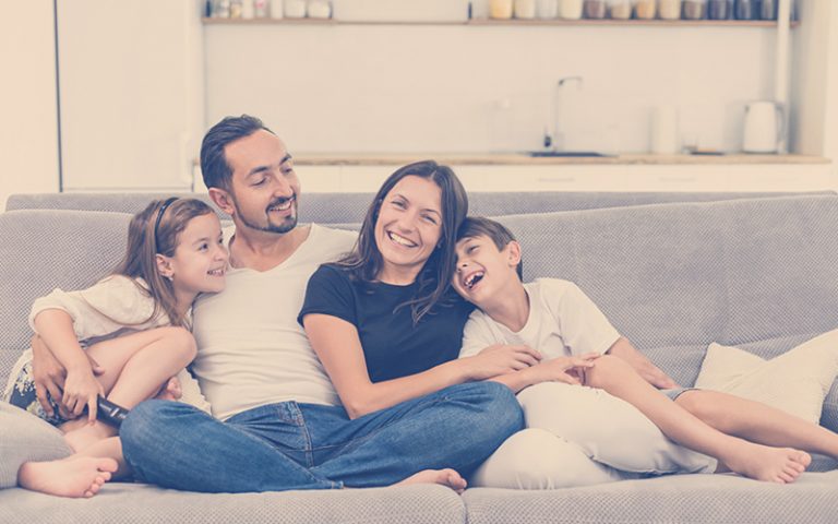 Familia en casa sentados en el sofá teniendo una sana convivencia familiar