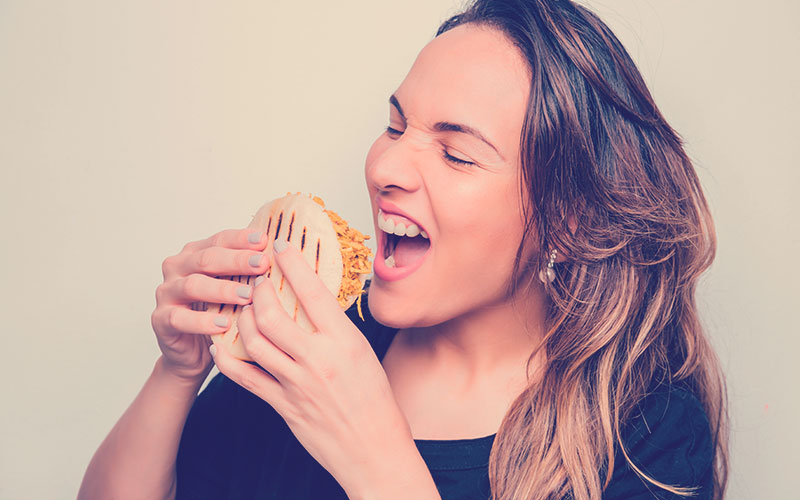 Niña latina sostiene una arepa en sus manos lista para comerla, Arepa rellena de pollo