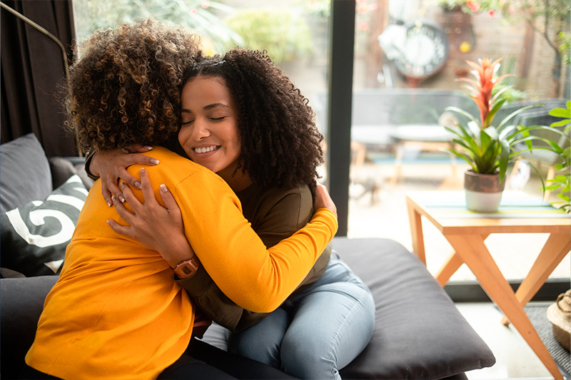 Una psicoterapeuta afroamericana consuela a la paciente adolescente abrazándola.