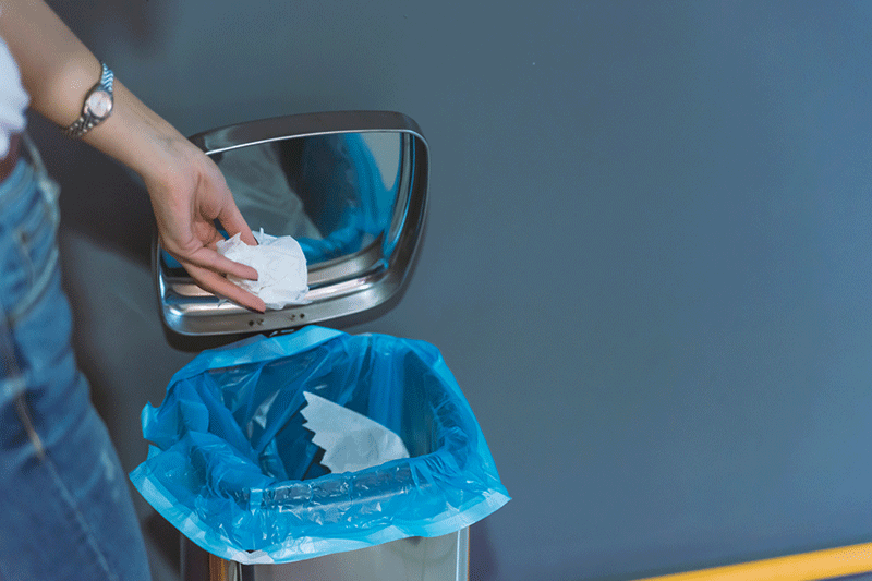 una mano sostiene el papel higienico para empapar la basura 